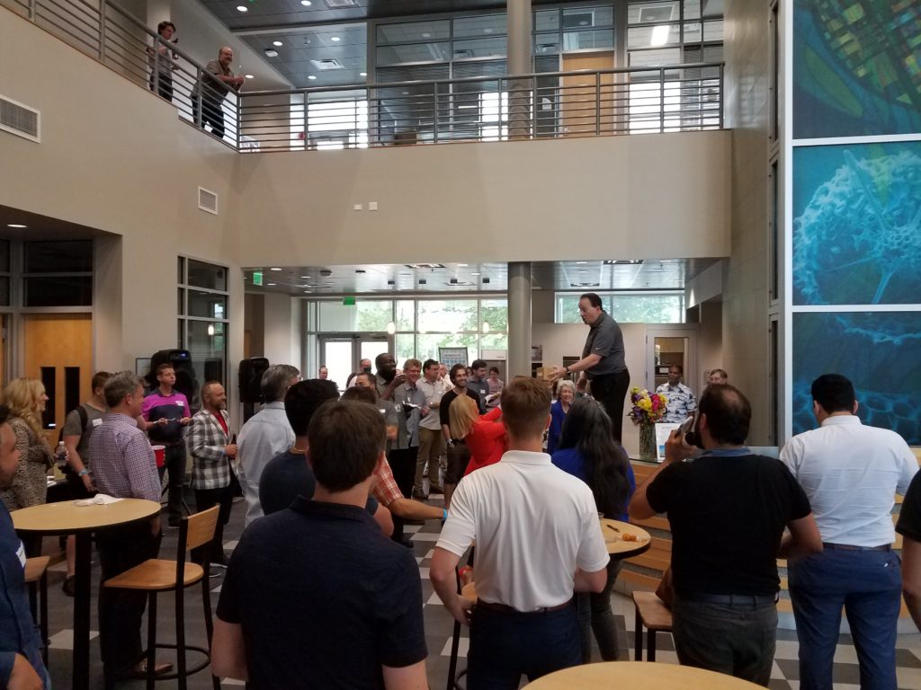 A crowd gathered for the first Third Thursday at The Hub, a gathering for entrepreneurs, surrounds Mark Long, who is standing on the reception desk.