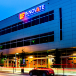 a nighttime image of UF Innovate | Accelerate at The Hub. The sign and the lower part of the building are lit against a dark blue sky.