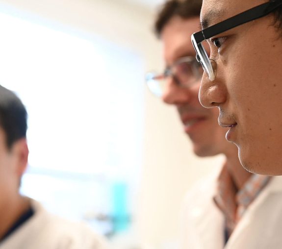 People in lab coats looking at something attentively.