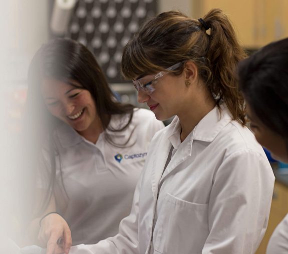 People in lab coats smiling as they observe a discovery in the lab.