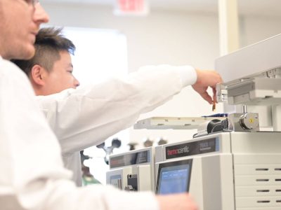 People adding a small test tube and analyzing samples from a batch using a machine.
