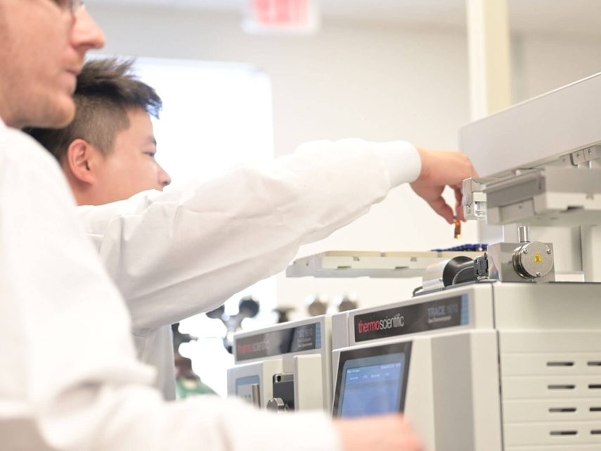 People adding a small test tube and analyzing samples from a batch using a machine.