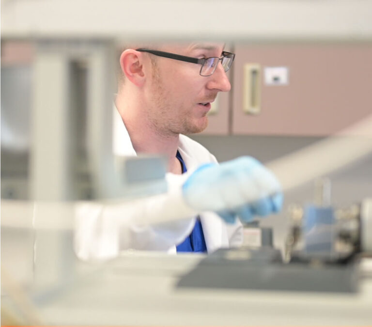 A person in a lab coat and gloves working with scientific equipment.