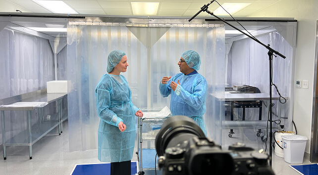Two people in blue disposable lab coats discussing something in the lab.